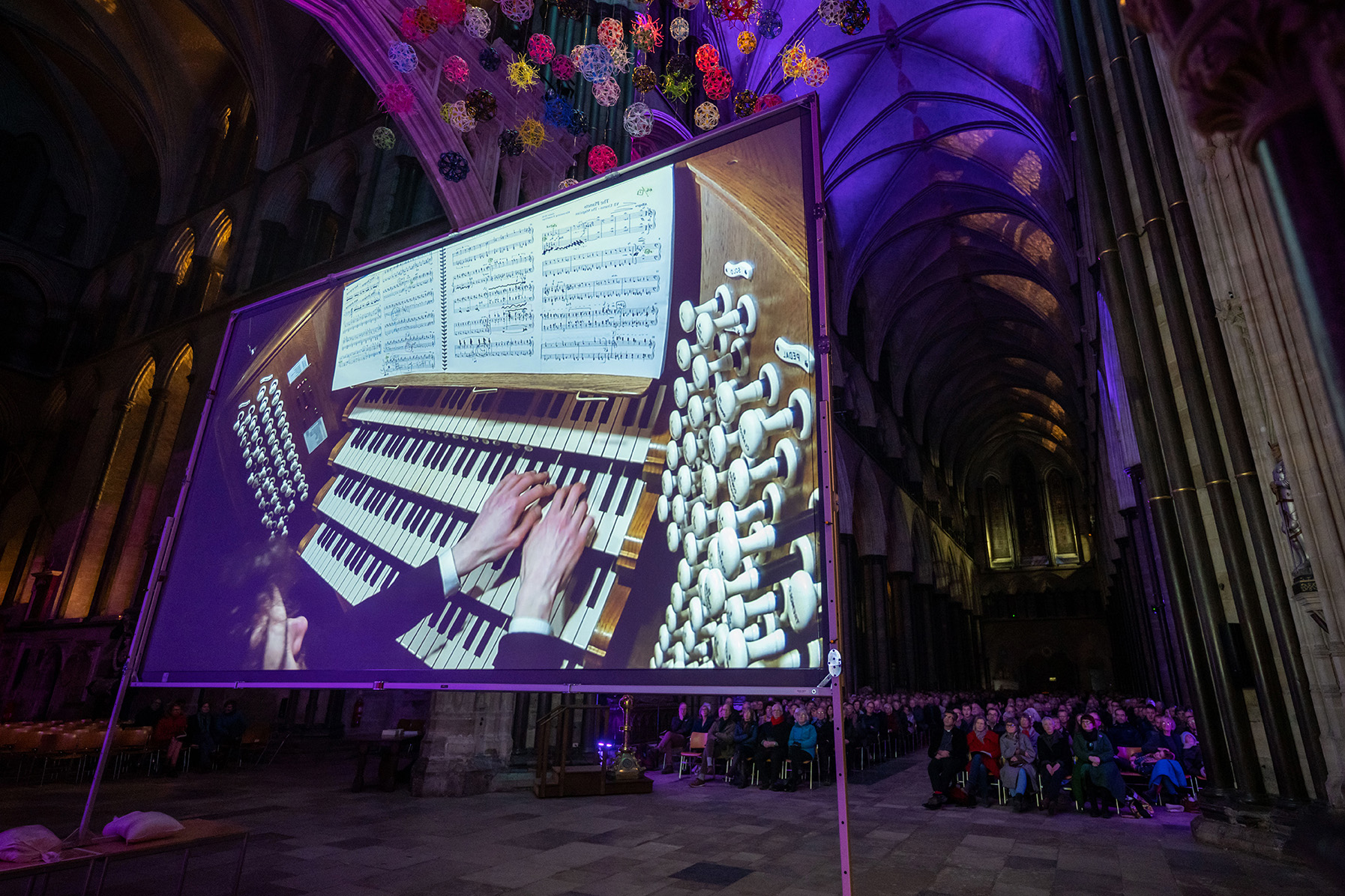 Person playing the organ projected on a screen in front of a large audience
