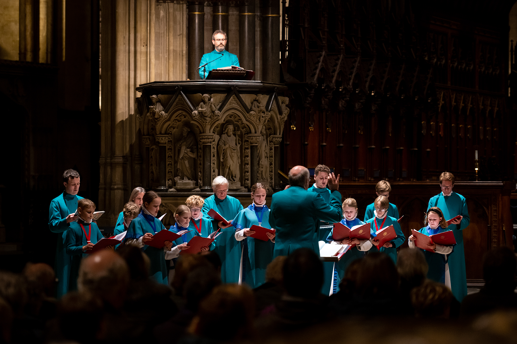 Salisbury Cathedral Choir in cassocks singing, being conducted by a man