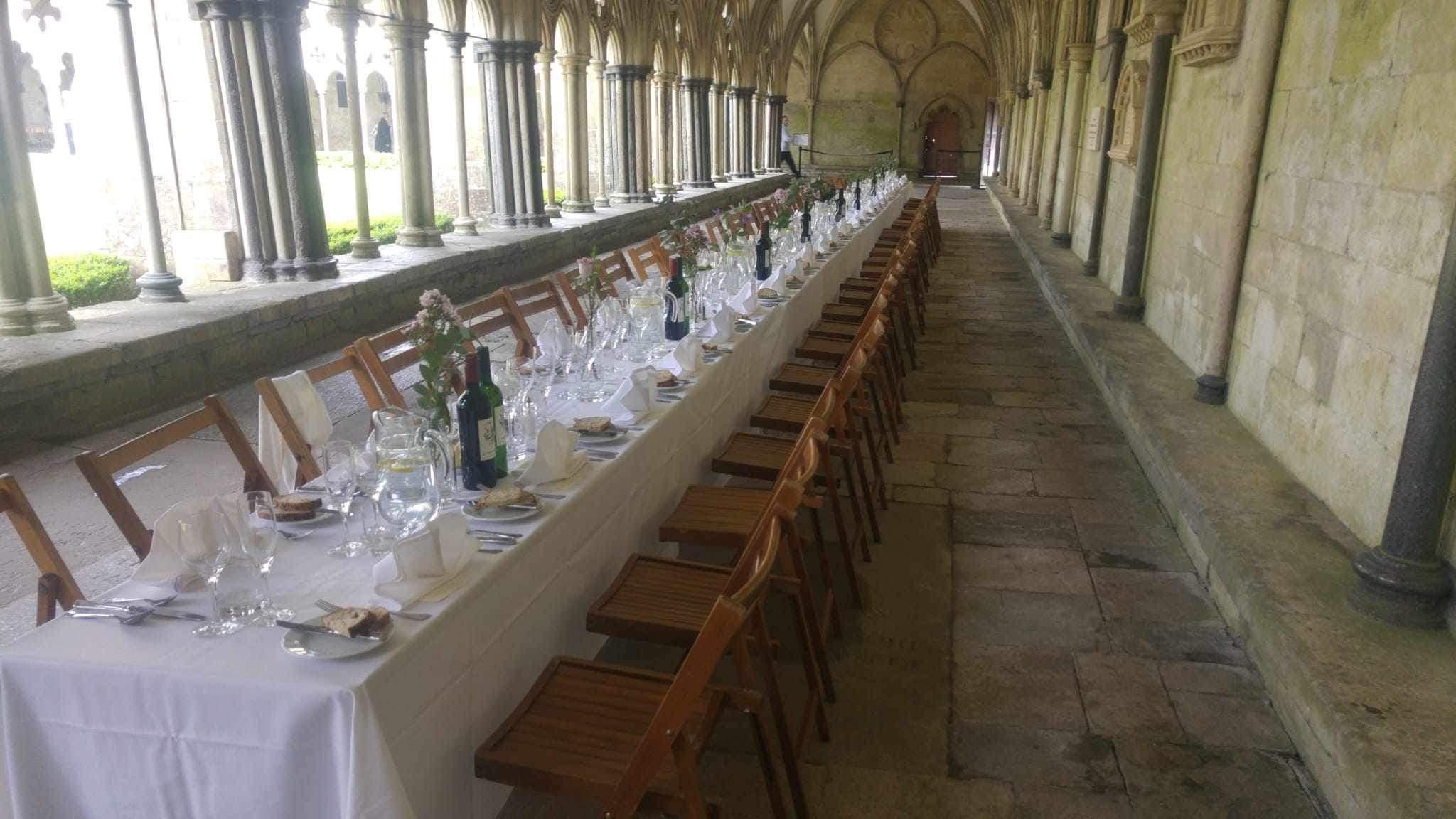 Long table set with table cloth and glasses along a cloister arm