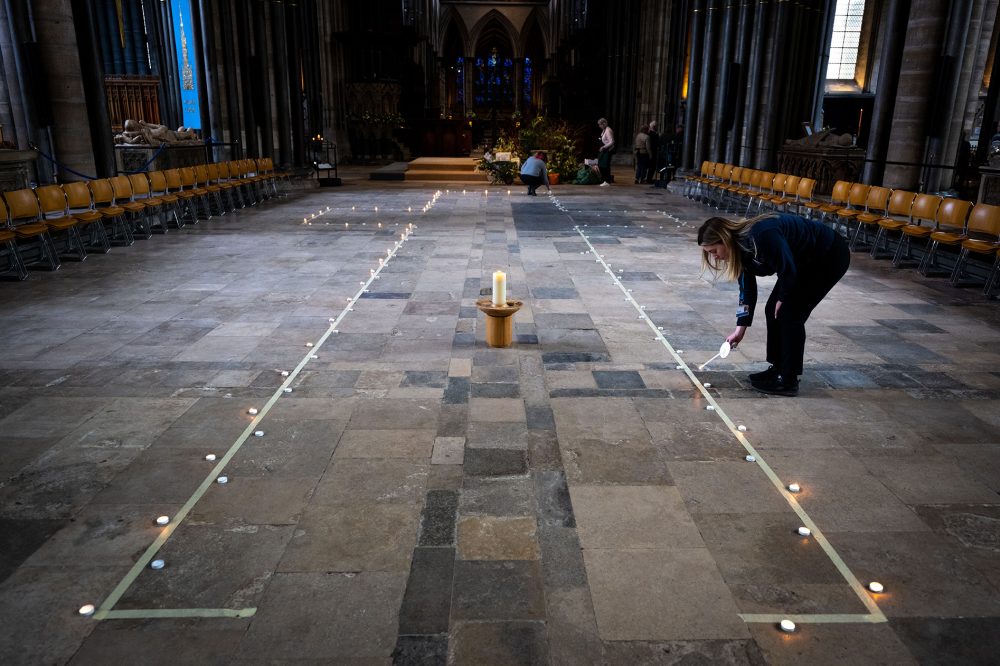 A line of candles marking out a cross on the floor. A woman is lighting a candle on the edge.