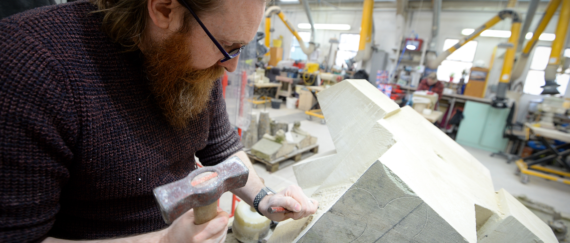 Man holding a tool working on carving a stone