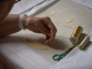 an embroiderer works with gold thread on a piece using the old Opus Anglicanum technique