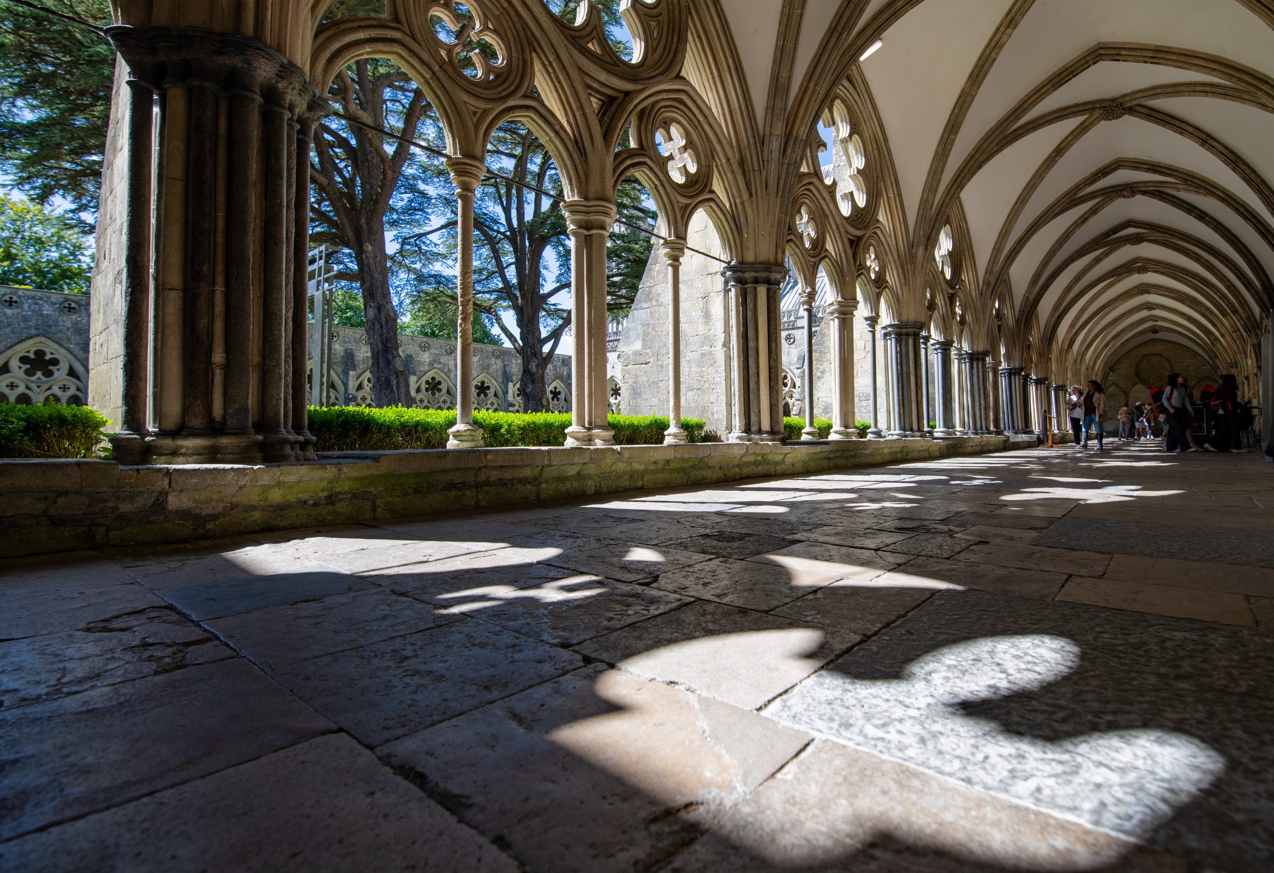 A wide view of the East Cloister with the sun spilling through the arches onto the stone floor.