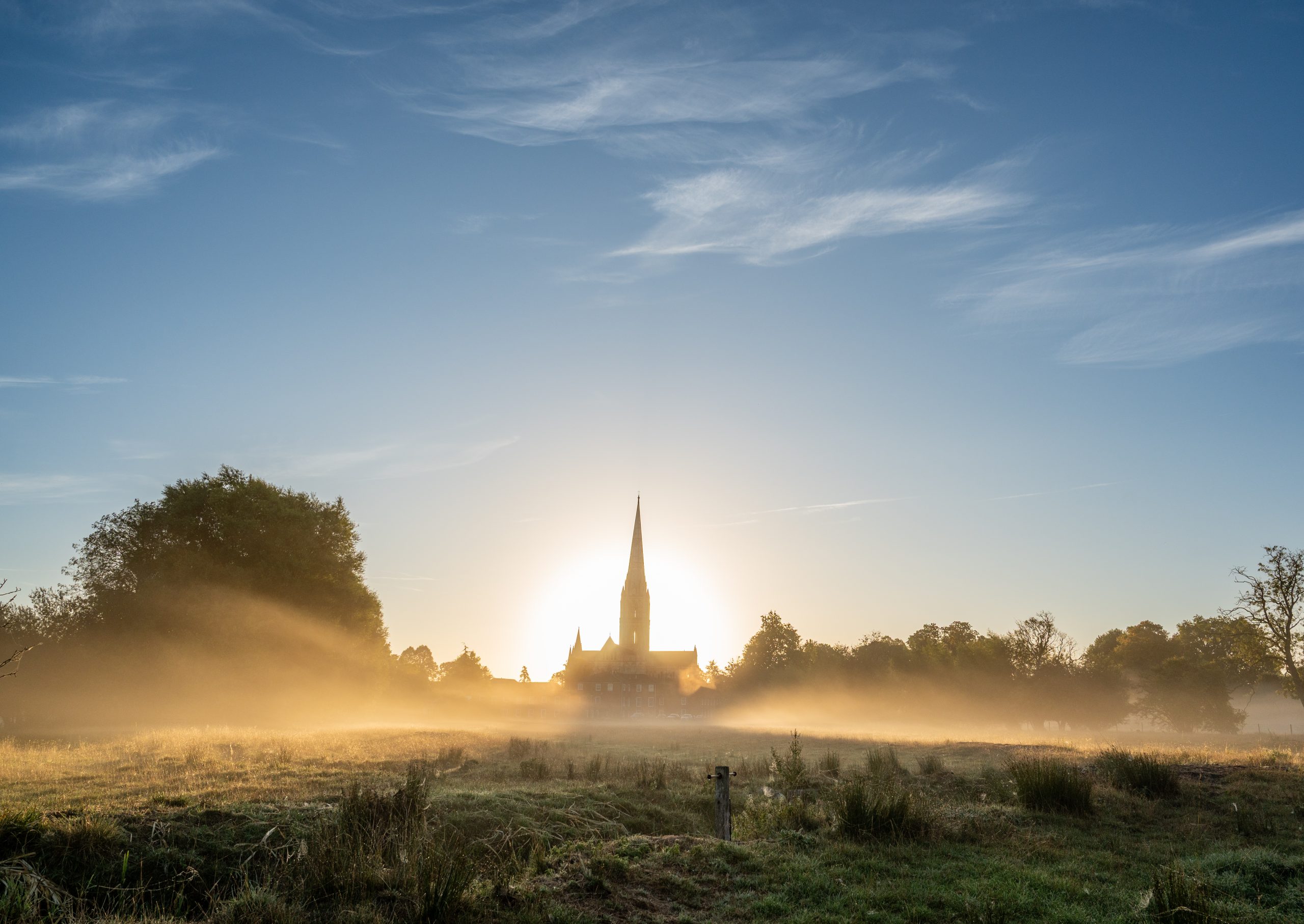 The Cathedral seen at sunrise from across the watermeadows in the West, with the light haloed behind the building.