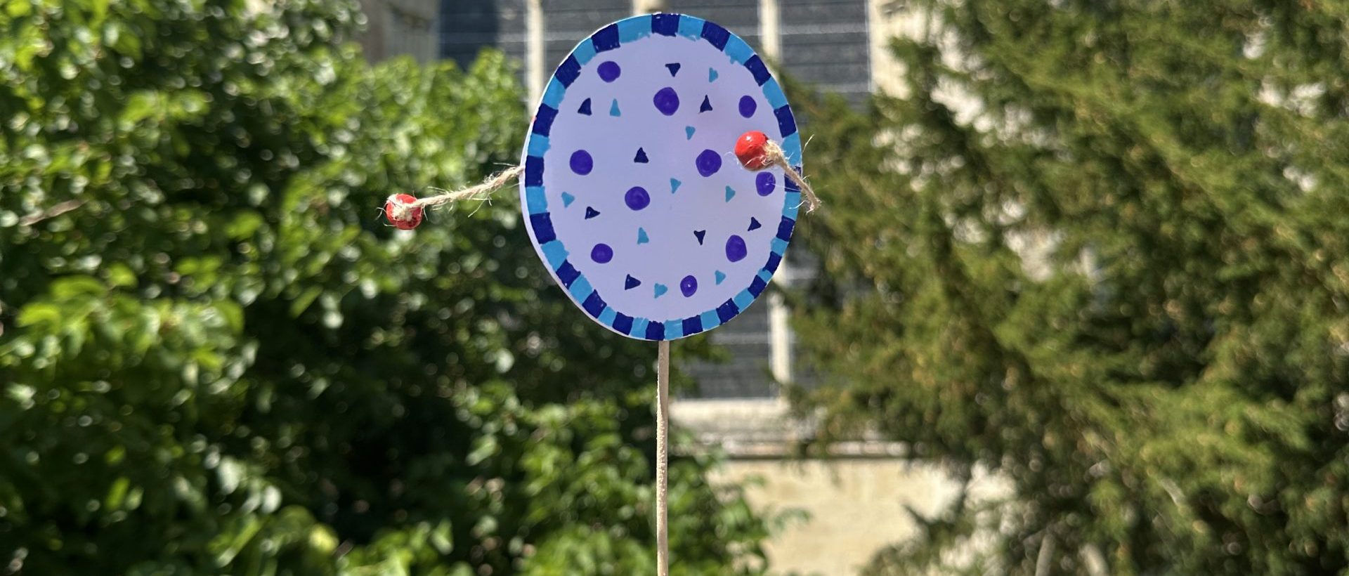 Photo shows a handmade paper 'clapper' instrument being twirled in the sunshine outside of the Cathedral Chapterhouse